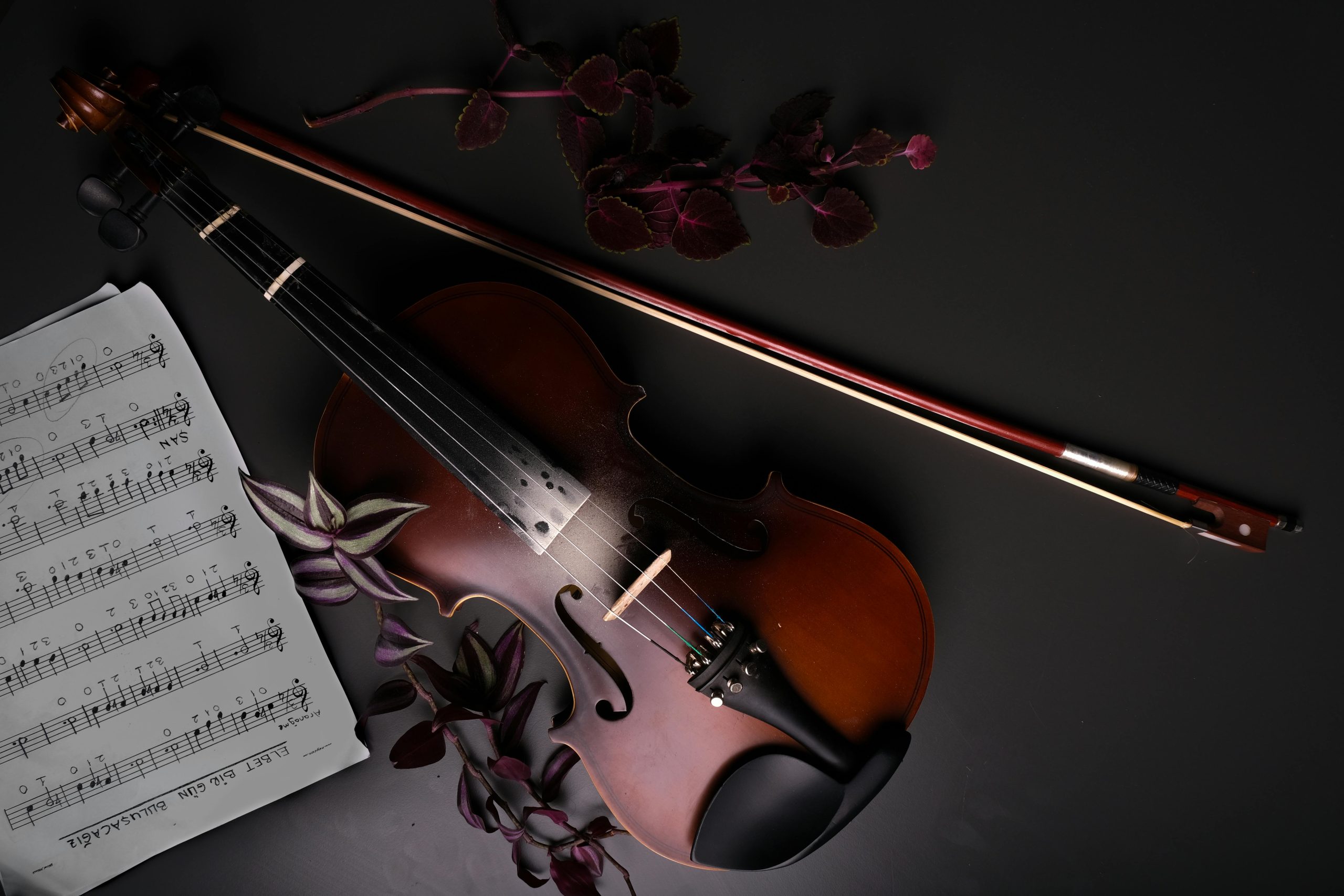Elegant still life featuring a violin, bow, and music sheet on a dark background.