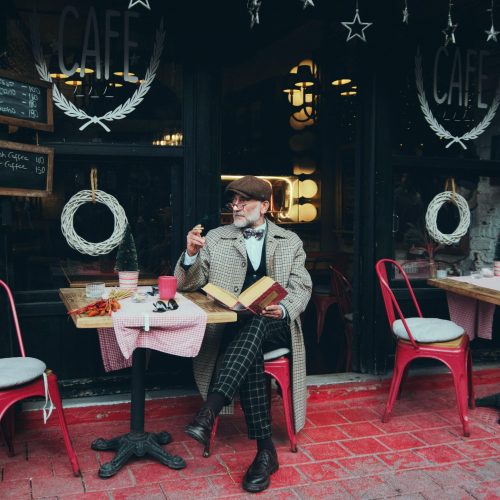 An elegantly dressed man with a book and coffee at a charming outdoor café in Istanbul, Türkiye.